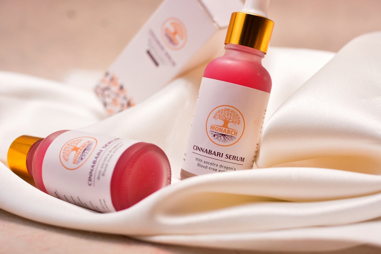 Elegant close-up of Cinnabari serum bottles on white fabric, showcasing luxury skincare packaging.