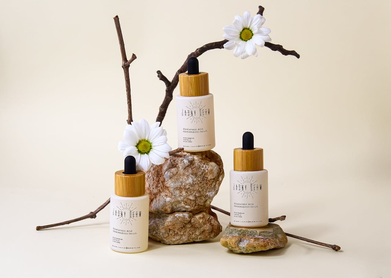 gallery-1 Organic hyaluronic acid serum bottles with floral and stone arrangement on neutral background.