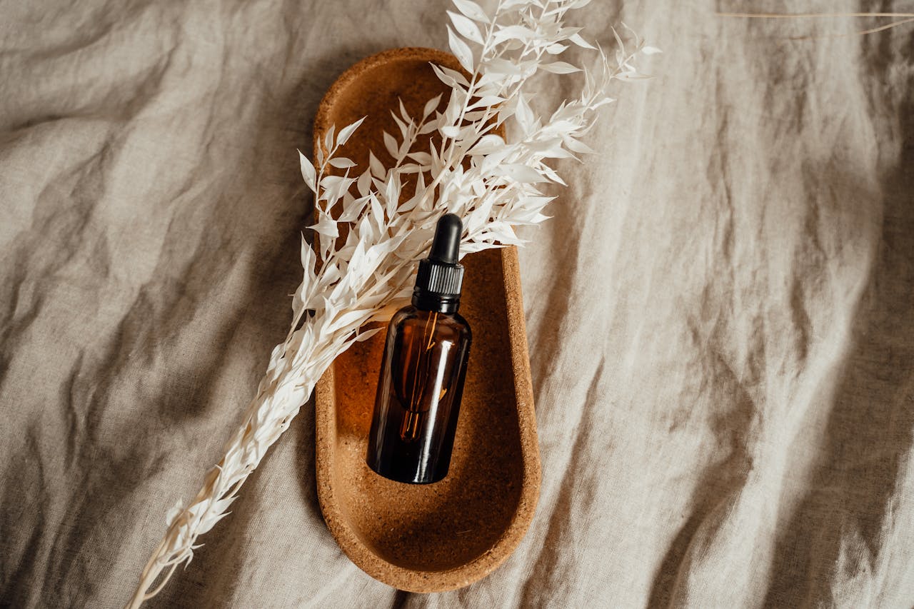 A stylish brown bottle with dropper on a wooden tray, resting on linen, with dried floral accents for a natural look.