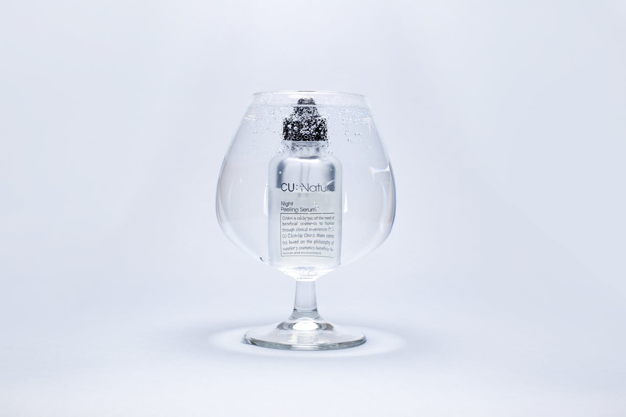 gallery-3 A luxury serum bottle submerged in a large wine glass filled with water, showcasing purity and elegance.